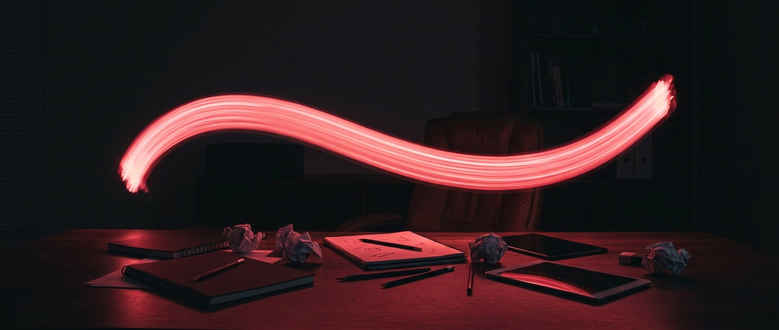 Luminous red brushstroke of light suspended above a designer desk in the dark
